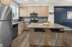 Modern kitchen featuring stainless steel appliances, light wood-finish cabinetry, a large center island with a stone-finish countertop, and wood-finish flooring - 