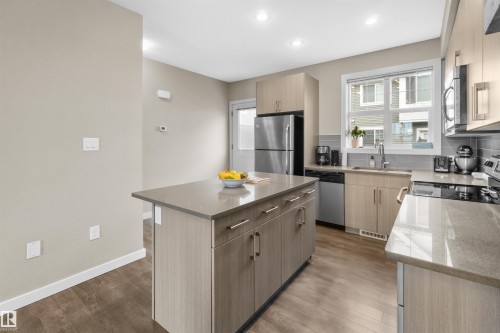 Contemporary kitchen featuring wood-finish cabinetry, a central island with storage, stainless steel appliances, a grey subway tile backsplash, and light-toned countertops - 13 2803 James Mowatt Trail, Edmonton, AB 