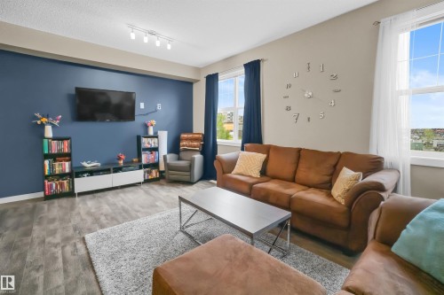 Spacious living area featuring plank wood-finish flooring, a contemporary track lighting fixture, and two large windows with white trim - 13 2803 James Mowatt Trail, Edmonton, AB 