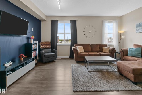 Spacious living area featuring wood-finish flooring, track lighting, and a painted accent wall - 13 2803 James Mowatt Trail, Edmonton, AB 