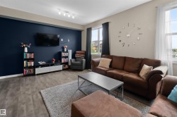 Living area featuring wood-finish flooring, a feature wall with a television mount, and two windows with dark and sheer curtain options - 