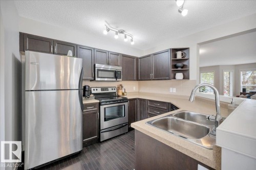 Kitchen featuring dark wood-finish cabinetry & stainless steel appliances - 4865 Terwillegar Common, Edmonton, AB - Indoor Photo Showing Kitchen With Double Sink