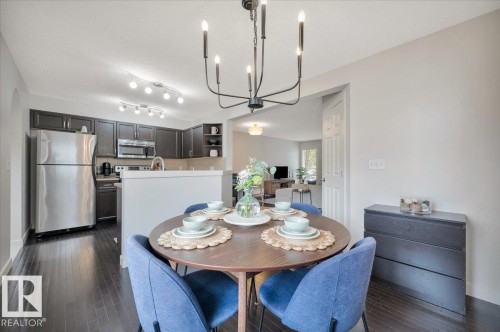 Dining area featuring a contemporary chandelier, wood-finish flooring, and a partial wall opening to the kitchen - 4865 Terwillegar Common, Edmonton, AB - Indoor Photo Showing Dining Room
