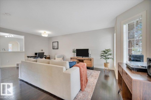 Spacious living area featuring dark wood-finish flooring and ample natural light from a large window with blinds - 4865 Terwillegar Common, Edmonton, AB - Indoor Photo Showing Living Room