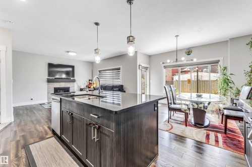 Open-concept kitchen featuring an island with built-in sink and stainless-steel dishwasher, dark wood-finish cabinetry, and pendant lighting - 8516 216 Street, Edmonton, AB 