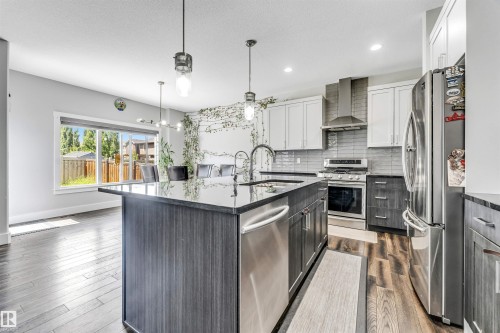 Kitchen featuring a large island with dark countertop, stainless steel appliances, and a tiled backsplash - 8516 216 Street, Edmonton, AB 