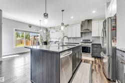 Kitchen featuring a large island with dark countertop, stainless steel appliances, and a tiled backsplash - 