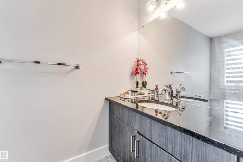 Bathroom vanity featuring dark wood-finish cabinetry, a black stone countertop, and an undermount sink with chrome fixtures - 8516 216 Street, Edmonton, AB 