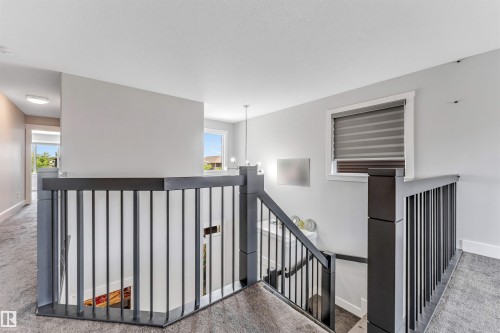 Upper-level landing featuring durable carpet flooring, a contemporary iron railing, and a window with blinds - 8516 216 Street, Edmonton, AB 