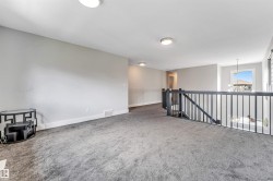 Spacious upper-level landing featuring plush grey carpeting, white baseboards, and light grey wall paint - 