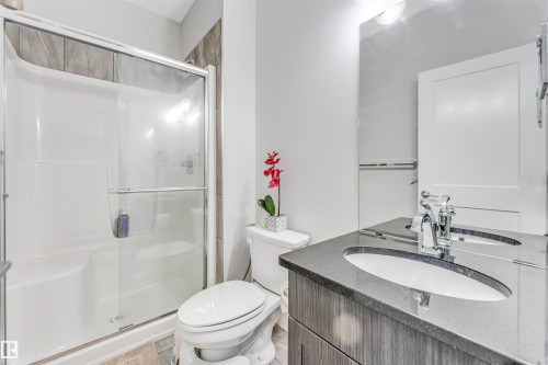 Bathroom featuring a shower stall with sliding glass doors, a vanity with a dark countertop and integrated sink, chrome fixtures, and a white toilet - 8516 216 Street, Edmonton, AB 