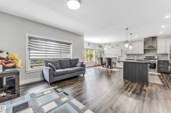 Open-concept living space featuring wood-finish flooring throughout, a modern kitchen with a large island and stainless steel appliances, and a dining area with pendant lighting - 