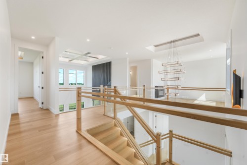 Upper-level landing featuring light wood-finish flooring, a contemporary chandelier, a glass and wood railing system, a tray ceiling with recessed lighting, and large windows - 1180 Genesis Lake Boulevard, Stony Plain, AB 