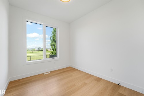 Bright interior space featuring a large window, light wood-finish flooring, white baseboards, and a contemporary ceiling light fixture - 1180 Genesis Lake Boulevard, Stony Plain, AB 