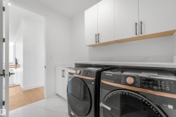 Dedicated laundry area featuring white upper cabinetry with matte black hardware, a wood-finish accent shelf, and a light-toned countertop - 
