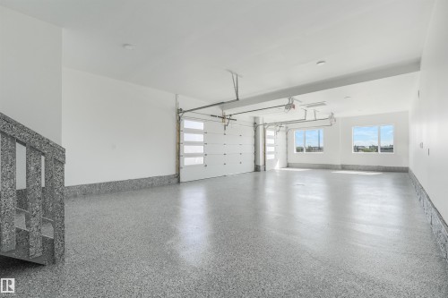 Spacious garage featuring a speckled epoxy floor finish, two modern garage doors with clear paneling, and ample natural light from multiple windows - 1180 Genesis Lake Boulevard, Stony Plain, AB 