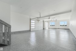 Spacious garage featuring a speckled epoxy floor finish, two modern garage doors with clear paneling, and ample natural light from multiple windows - 
