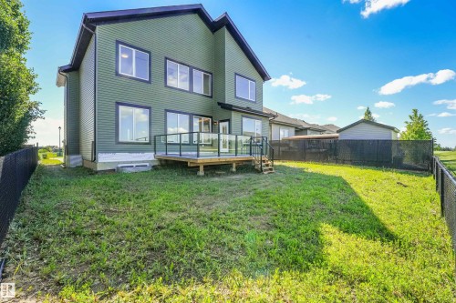 Rear exterior featuring green horizontal siding, multiple large windows with dark trim, and a raised wood deck with glass panel railings - 1180 Genesis Lake Boulevard, Stony Plain, AB 