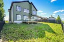 Rear exterior featuring green horizontal siding, multiple large windows with dark trim, and a raised wood deck with glass panel railings - 1180 Genesis Lake Boulevard, Stony Plain, AB 
