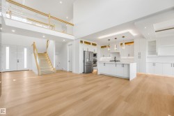 Open-concept living space with light wood-finish flooring, a contemporary kitchen featuring stainless steel appliances and a center island, and a dual-height ceiling - 