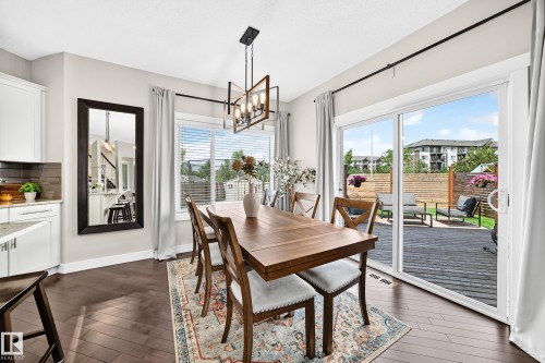 Dining area featuring dark wood-finish flooring, a contemporary rectangular chandelier, and a large sliding glass door opening to an outdoor deck - 13724 166 Avenue Nw, Edmonton, AB 