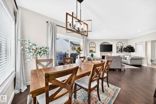 Open-concept living area featuring dark wood-finish flooring, recessed lighting, and a contemporary linear chandelier with a wood and metal frame - 13724 166 Avenue Nw, Edmonton, AB 