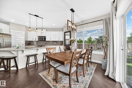 Open-concept living space featuring wood-finish flooring, a kitchen island with stone countertop, stainless steel appliances, and a dining area with a contemporary chandelier - 13724 166 Avenue Nw, Edmonton, AB 