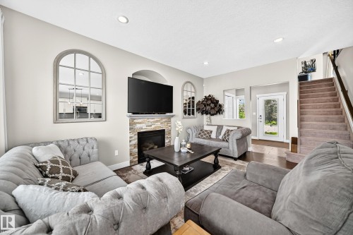 Living area featuring a stone-clad fireplace with a mantel, recessed lighting, wood-finish flooring, a glass-paned exterior door, and carpeted stairs with a wood handrail - 13724 166 Avenue Nw, Edmonton, AB 