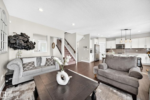 Open-concept living area featuring wood-finish flooring, recessed lighting, a modern kitchen with white cabinetry, a kitchen island, and a stainless steel refrigerator - 13724 166 Avenue Nw, Edmonton, AB 