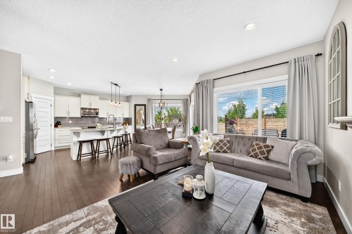 Open-concept living space featuring wood-finish flooring, recessed lighting, expansive windows with blinds, a kitchen island with seating, and pendant lighting - 13724 166 Avenue Nw, Edmonton, AB 
