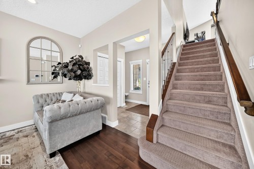 Warm entryway featuring wood-finish flooring, a carpeted staircase with wood handrails, neutral wall tones, recessed lighting, and a window - 13724 166 Avenue Nw, Edmonton, AB 