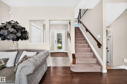 Hardwood flooring extending from the living area, a welcoming entryway with tiled flooring, a glass-paneled front door, and a carpeted staircase with a dark wood handrail and black metal balusters - 13724 166 Avenue Nw, Edmonton, AB 