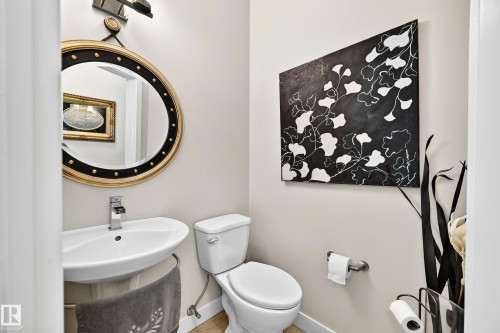 Pedestal sink with chrome faucet, circular mirror with decorative gold and black frame, wall-mounted light fixture, and tile flooring - 13724 166 Avenue Nw, Edmonton, AB 