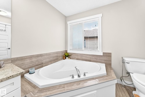 Corner soaking tub featuring chrome fixtures, surrounded by a tile deck and wainscoting - 13724 166 Avenue Nw, Edmonton, AB 