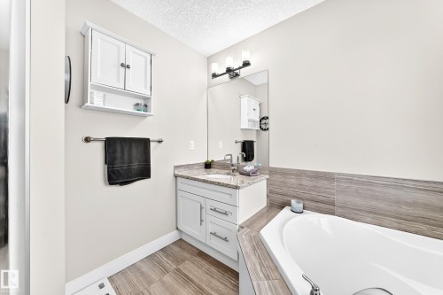 Bathroom featuring a built-in tub with tile surround, a vanity with granite countertop and undermount sink, a wall-mounted medicine cabinet, a mirror, and wood-finish flooring - 13724 166 Avenue Nw, Edmonton, AB 