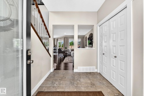 Entryway featuring tile flooring, a multi-paneled bifold closet door, and a staircase with wood railing and metal balusters - 13724 166 Avenue Nw, Edmonton, AB 