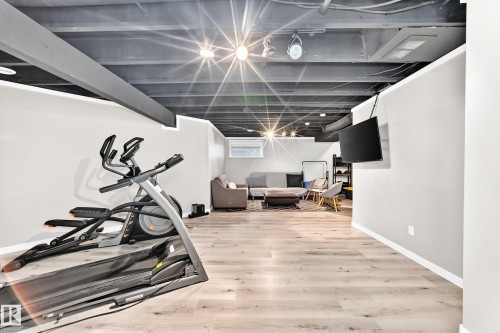 Finished lower level featuring wood-finish flooring, recessed lighting, a mounted television, and painted exposed ceiling beams - 13724 166 Avenue Nw, Edmonton, AB 
