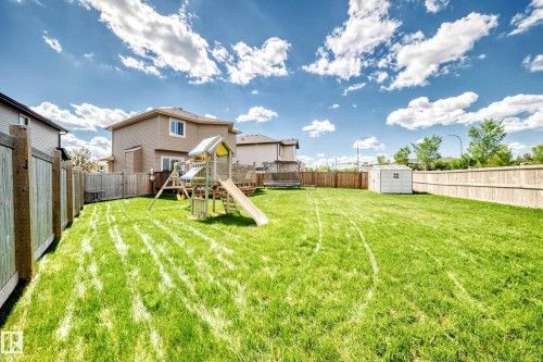 Expansive fenced backyard featuring a large green lawn, a white storage shed, and a playset with slide - 13724 166 Avenue Nw, Edmonton, AB 