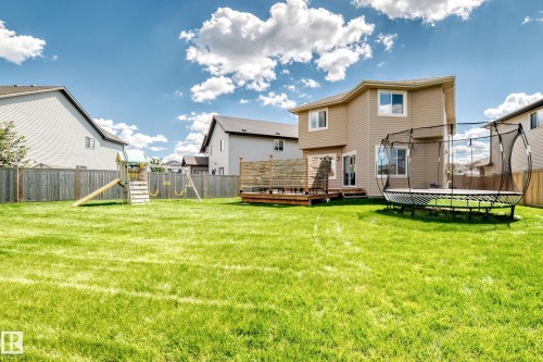 Expansive fenced backyard featuring a wood-plank deck, exterior siding, and a large green lawn - 13724 166 Avenue Nw, Edmonton, AB 