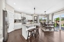 Open-concept kitchen and dining area featuring white cabinetry, stainless steel appliances, a center island with a stone countertop, and wood-finish flooring - 13724 166 Avenue Nw, Edmonton, AB 