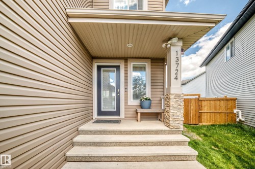 Inviting front entry featuring a glass-paneled door, concrete steps, and a stone-clad pillar - 13724 166 Avenue Nw, Edmonton, AB 