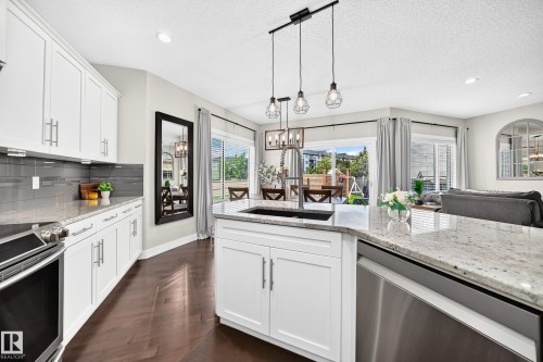 Kitchen featuring white cabinetry, light-toned countertops, a dark-finish backsplash, dark wood-finish flooring, and stainless steel appliances - 13724 166 Avenue Nw, Edmonton, AB 