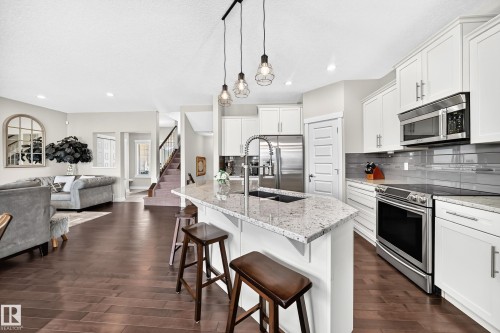 Modern kitchen featuring white cabinetry, stainless steel appliances, a white stone countertop island with an undermount sink, and pendant lighting - 13724 166 Avenue Nw, Edmonton, AB 