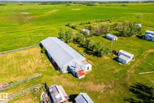 Expansive agricultural property featuring a large barn with a metal roof, multiple outbuildings, fenced enclosures, vast green fields, and mature trees - 551027 Range Road 193, Rural Lamont County, AB 