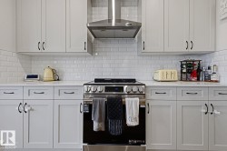 Contemporary kitchen featuring light-toned cabinetry with dark hardware, white subway tile backsplash, stainless steel range with overhead vent hood, and light-toned countertops - 