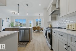 Contemporary kitchen featuring light wood-finish flooring, white cabinetry with black hardware, and stainless steel appliances - 