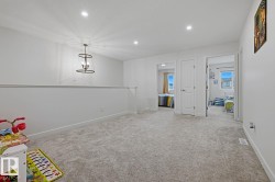 Carpeted loft area featuring a contemporary dark-finish chandelier, recessed ceiling lighting, white walls, and bright doorways to additional rooms - 