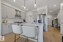 Contemporary kitchen featuring light gray shaker cabinetry, stainless steel appliances, a subway tile backsplash, recessed lighting, and wood-finish flooring - 