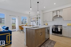 Open-concept kitchen featuring an island with a double basin sink, light-toned wood-finish flooring, white subway tile backsplash, stainless steel appliances, and light grey cabinetry - 