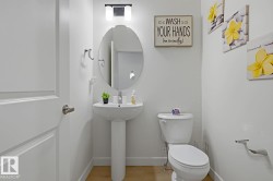 Pedestal sink with an oval mirror, wall-mounted lighting, and a white toilet - 